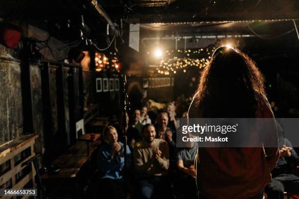 rear view of female stand-up comedian performing for multiracial audience at illuminated theater - stand up comedy stockfoto's en -beelden