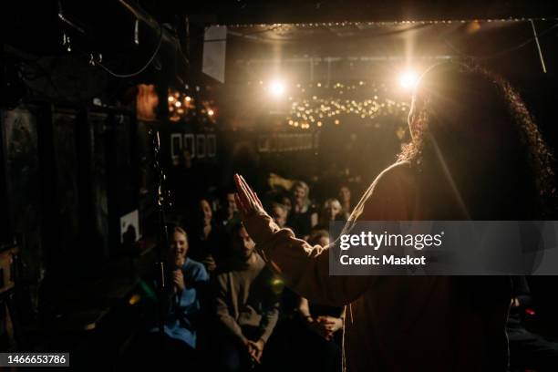 female stand-up comedian performing for multiracial audience at illuminated stage theater - comedian foto e immagini stock