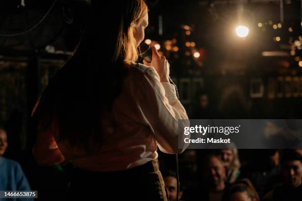 rear view of woman performing stand-up comedy for audience at amateur theater - stand up comedy stock-fotos und bilder