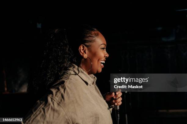 happy young woman with microphone performing stand-up comedy at theater - comedian fotografías e imágenes de stock