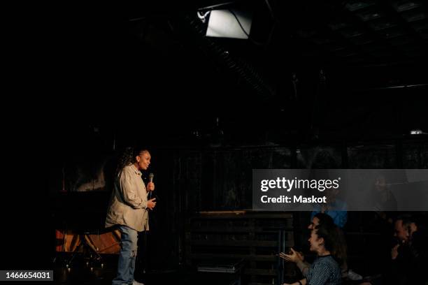 young woman performing stand-up comedy in front of audience on stage at theater - stand up comedian - fotografias e filmes do acervo