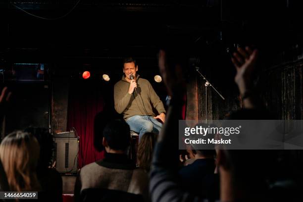 senior male comedian performing in front of audience on stage at theater - comedian foto e immagini stock