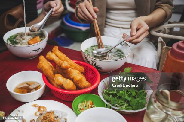 vietnamese  woman eating pho soup with fried breadstick in street restaurant - hanoi stockfoto's en -beelden