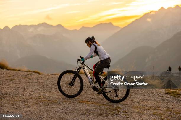 woman with long brown hair wearing sunglasses and a helmet riding up the mangart mountain. electric bicycle - motorcycle wheel stock pictures, royalty-free photos & images