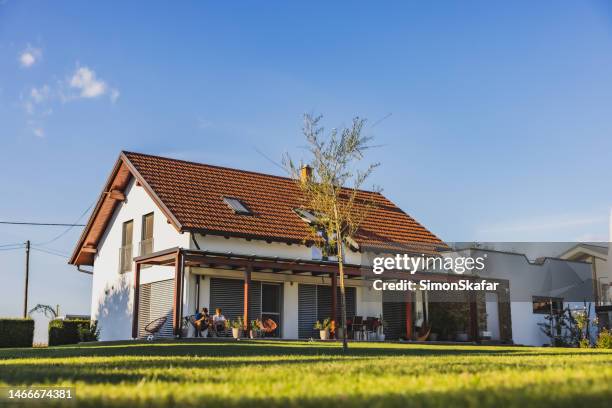 modern house with terrace on the countryside,two boys sitting on chairs on the terrace and using their phone,clear sky in the background - rural house stock pictures, royalty-free photos & images