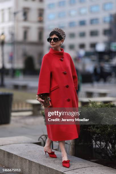 Fashion week guest seen wearing a red long coat, a bag by Carolina Herrera, an animal printed hat, shades by Loewe, golden jewelry and red heels...