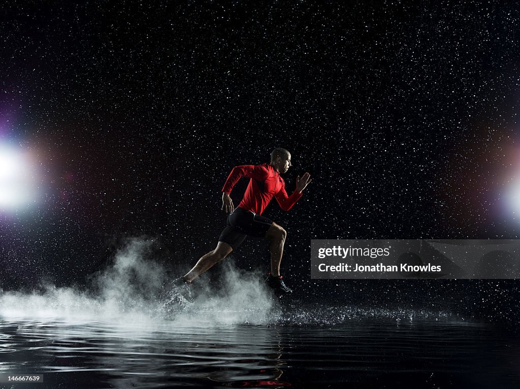 Athlete running in rain through water at night