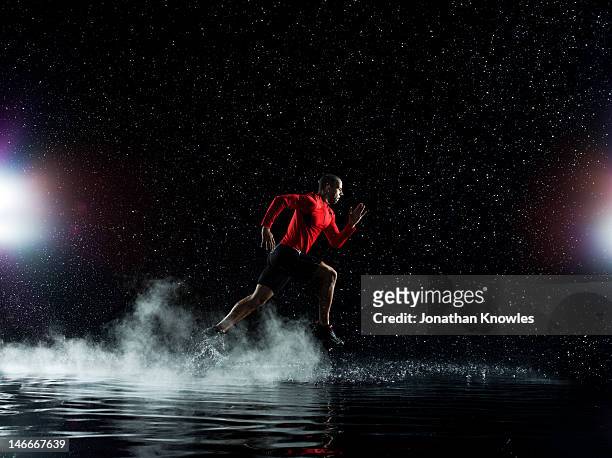 athlete running in rain through water at night - forward athlete stockfoto's en -beelden