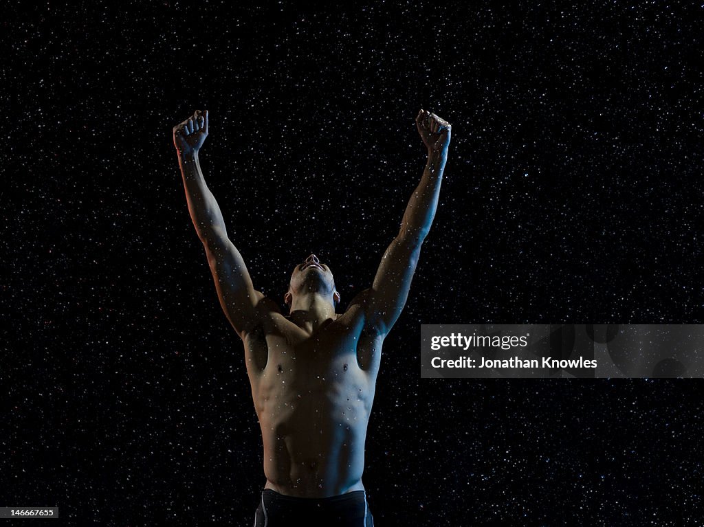 Male athlete raising arms in victory in rain