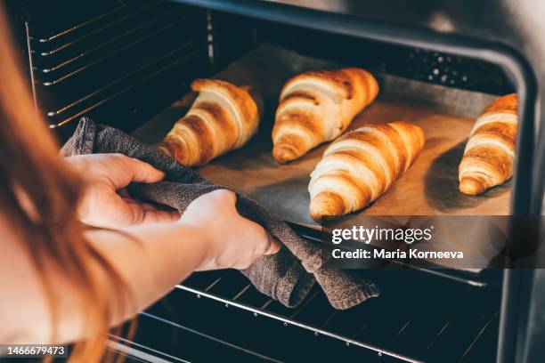 woman removing baked croissants tray from an oven. - backblech stock-fotos und bilder