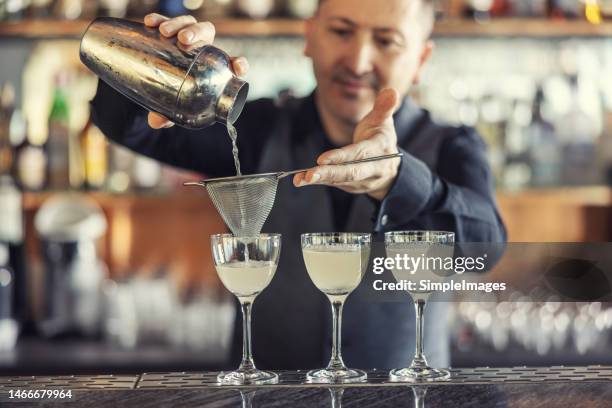 a professional bartender prepares cocktail drinks at the bar, pours the drink from a shaker through a strainer. - daiquiri stock pictures, royalty-free photos & images