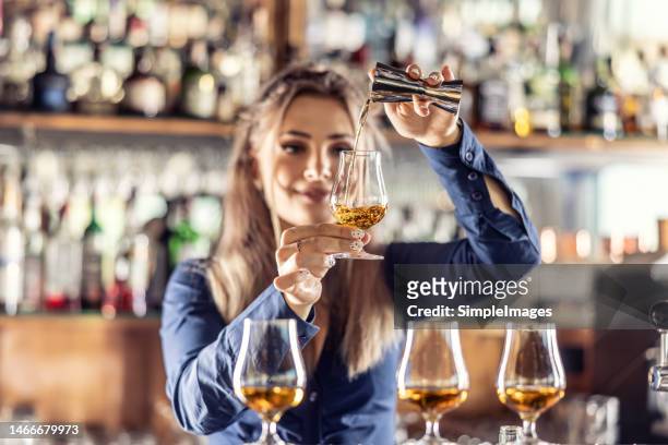 young female bartender professionally pours rum or brandy from steel jigger into glass at bar. - rum tasting stock pictures, royalty-free photos & images