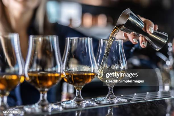young female bartender professionally pours rum or brandy from steel jigger into glass at bar. - rum sterkedrank stockfoto's en -beelden