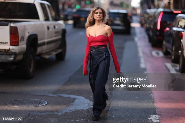 Xenia Adonts seen wearing a shoulder free red longsleeve shirt, a dark blue Otto Linger oversized jeans, black boots and a black Louis Vuitton bag...