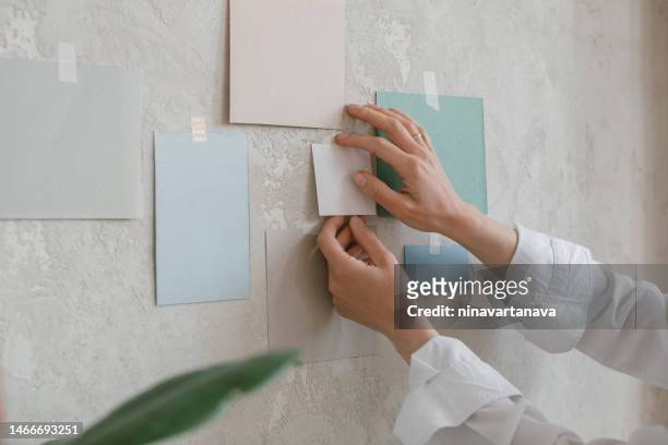 close-up of a woman taping colour paper samples to a wall - putting indoors stock pictures, royalty-free photos & images