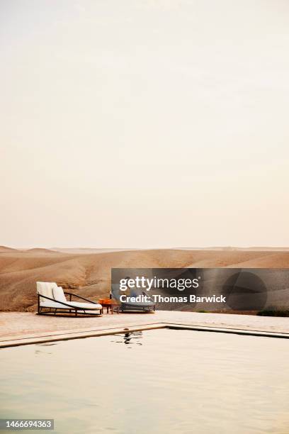 wide shot man sitting beside pool and working on laptop at desert camp - laptop desert stock pictures, royalty-free photos & images