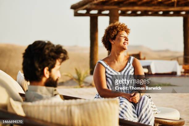 medium shot of smiling couple relaxing in lounge chairs at desert camp - desertman stock pictures, royalty-free photos & images