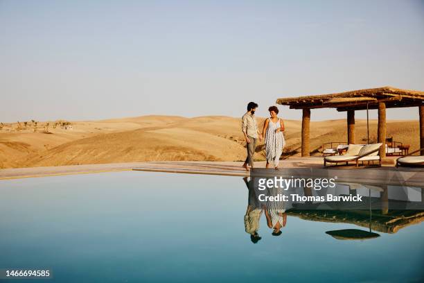 wide shot of couple walking around pool at desert camp at sunrise - couple dunes stockfoto's en -beelden