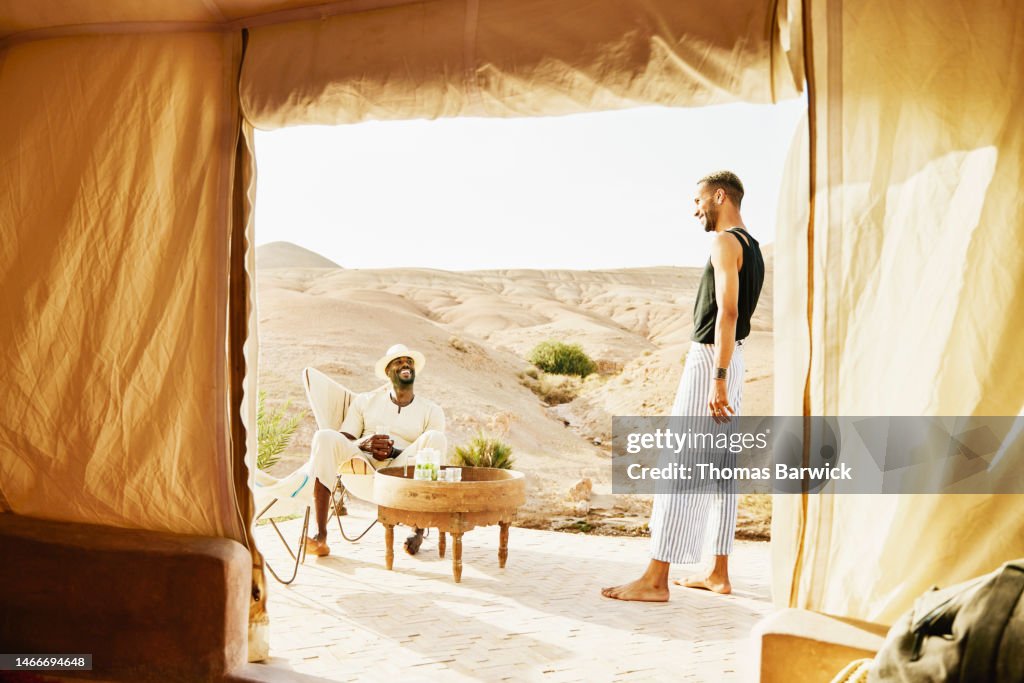 Wide shot smiling couple relaxing outside of tent while at desert camp
