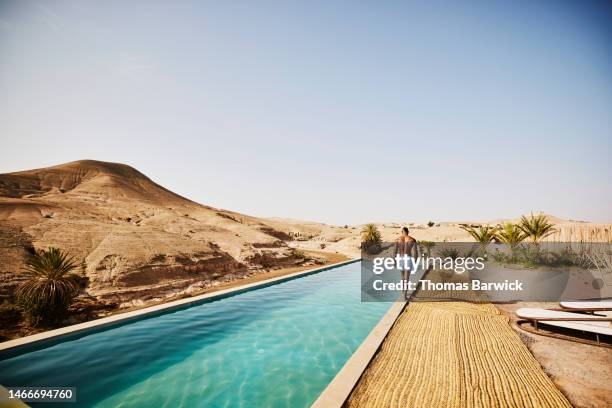 wide shot of man walking around edge of pool at moroccan desert camp - luxury hotel stock pictures, royalty-free photos & images