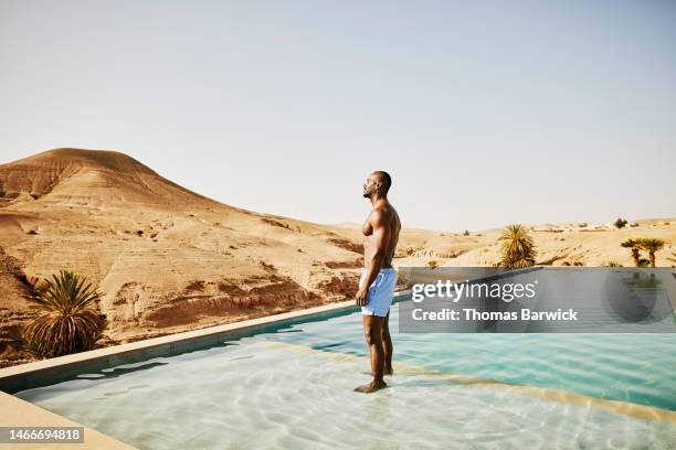 wide shot of man standing in pool while relaxing at desert camp - escapismo imagens e fotografias de stock