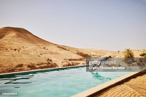 wide shot man diving into pool at moroccan desert camp during vacation - swimming pool hill stock pictures, royalty-free photos & images