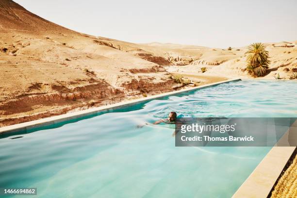 wide shot man swimming in pool at moroccan desert camp during vacation - travel fotografías e imágenes de stock