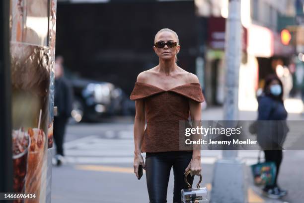 Fashion week guest seen wearing a brown shoulder free top, black leather pants, dark shades, black boots and a transparent bag before the Brandon...