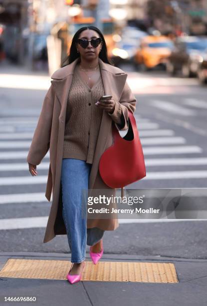 Fashion week guest seen wearing hearted shades, a red heart bag, jeans, a beige cardigan and beige coat with pink flats before the Brandon Maxwell...