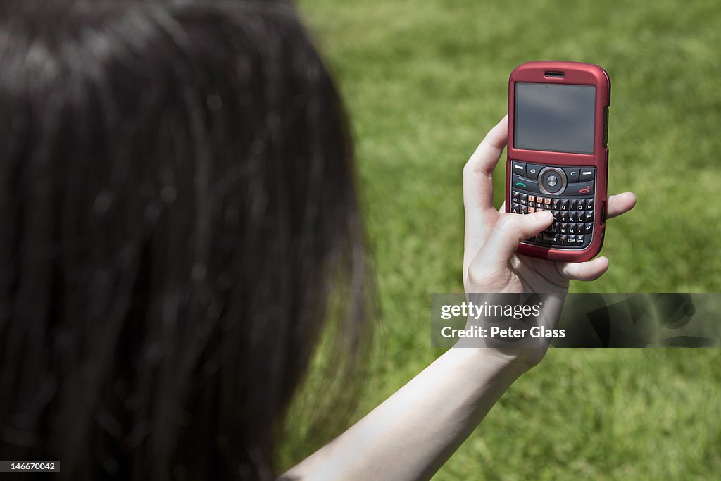 Eurasian teenage girl at a park with smart phone.