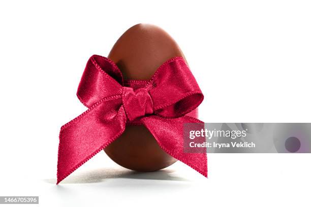 chocolate easter egg with silk ribbon in viva magenta color of the 2023 year on white background, isolated. - egg white background stock-fotos und bilder