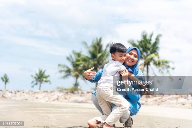 little boy hugging his mother - muslim woman beach stock-fotos und bilder