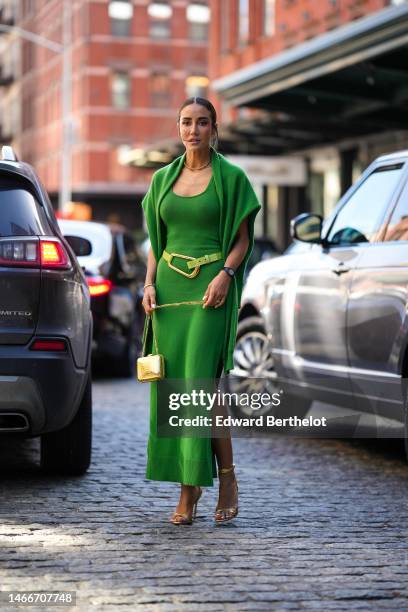 Tamara Kalinic wears diamond earrings, a gold and diamonds necklace, a green oversized wool pullover knot at the shoulder as a scarf, a matching...