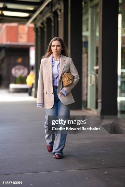 Iana Rad wears diamonds earrings, a navy blue and white striped print pattern shirt, a beige oversized blazer jacket, a white tank-top, a beige matte...