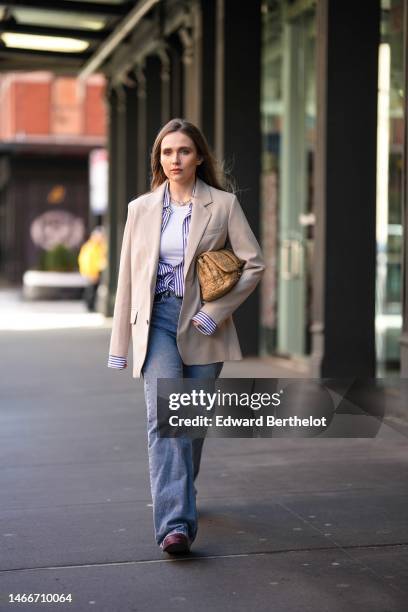 Iana Rad wears diamonds earrings, a navy blue and white striped print pattern shirt, a beige oversized blazer jacket, a white tank-top, a beige matte...