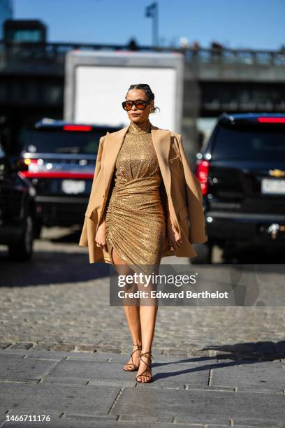 Sai De Silva wears black and orange sunglasses, silver earrings, a beige with embroidered gold sequined turtleneck / wraps short dress, a beige...