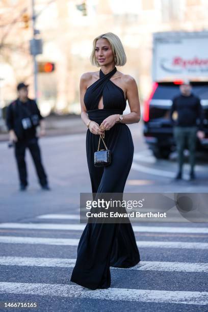 Guest wears gold earrings, a black halter-neck / cut-out chest / large belted wide legs pants, a black shiny leather snake print pattern clutch ,...