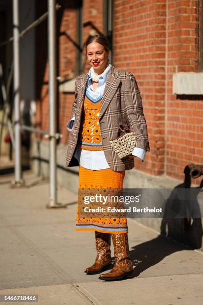Guest wears white pearls earrings, a white embroidered pearls large necklace, a pale blue shirt, an orange wool cut-out pattern with brown and blue...