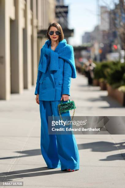 Guest wears navy blue sunglasses, a flashy blue braided wool pullover knot at the waist, a flashy blue blazer jacket, matching blue large suit pants,...