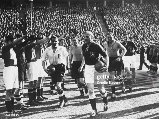 German team captain Fritz Szepan runs onto the field ahead of England team captain Eddie Hapgood flanked by both teams giving the Nazi salute before...