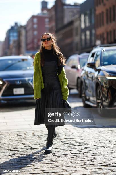 Guest wears black sunglasses, gold pendant earrings, a black turtleneck / long sleeves t-shirt, a black shiny leather square-neck / pleated midi...