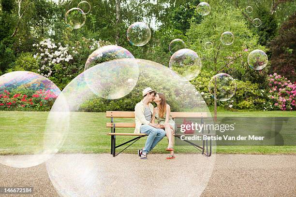 couple cuddling on bench, surrounded by bubbles. - teen dating stock pictures, royalty-free photos & images