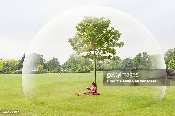 woman reading book in park in large bubble - protezione foto e immagini stock