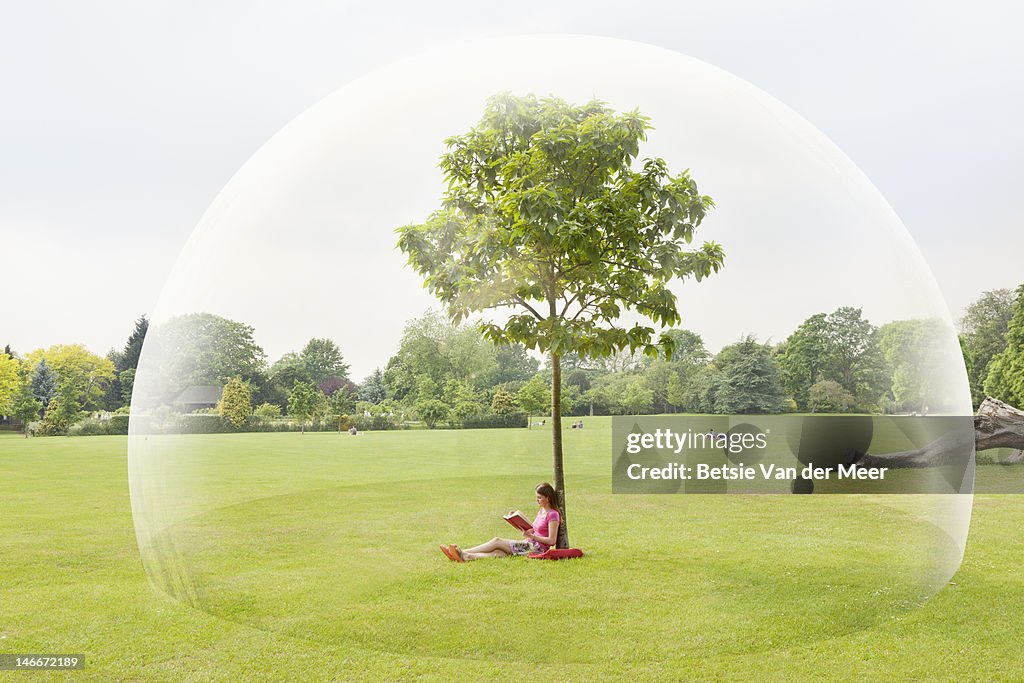 Woman reading book in park in large bubble