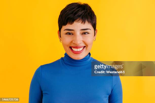 happy young woman with pixie haircut standing against yellow background - kurzes haar dame stock-fotos und bilder