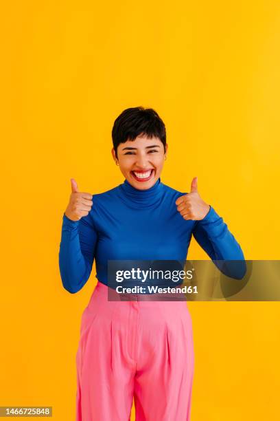 happy woman showing thumbs up against yellow background - happy woman thumbs studio ストックフォトと画像