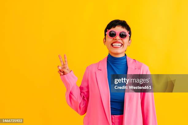 playful young woman wearing sunglasses gesturing against colored background - lady studio sonnenbrille stock-fotos und bilder