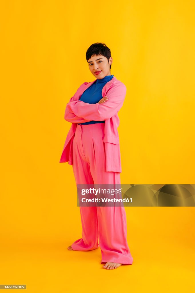 Confident young woman standing with arms raised over yellow background