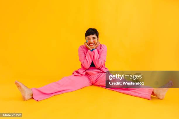 happy young woman sitting with legs apart in over yellow background - legs apart fotografías e imágenes de stock