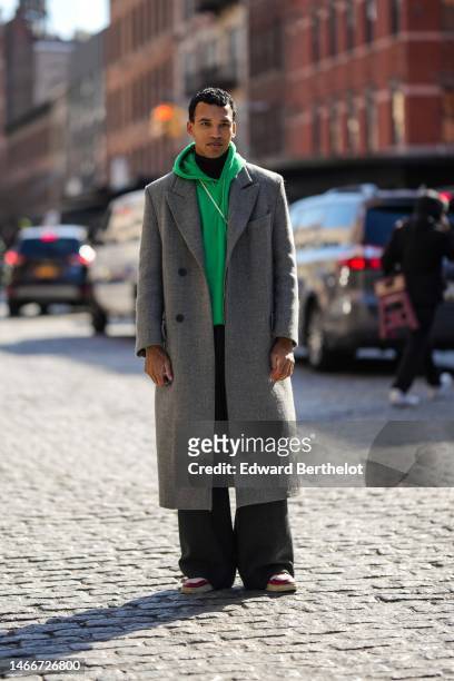 Guest wears a black turtleneck pullover, a green hoodie sweater, a pale gray long coat, black suit pants, white and burgundy shiny leather Air Force...